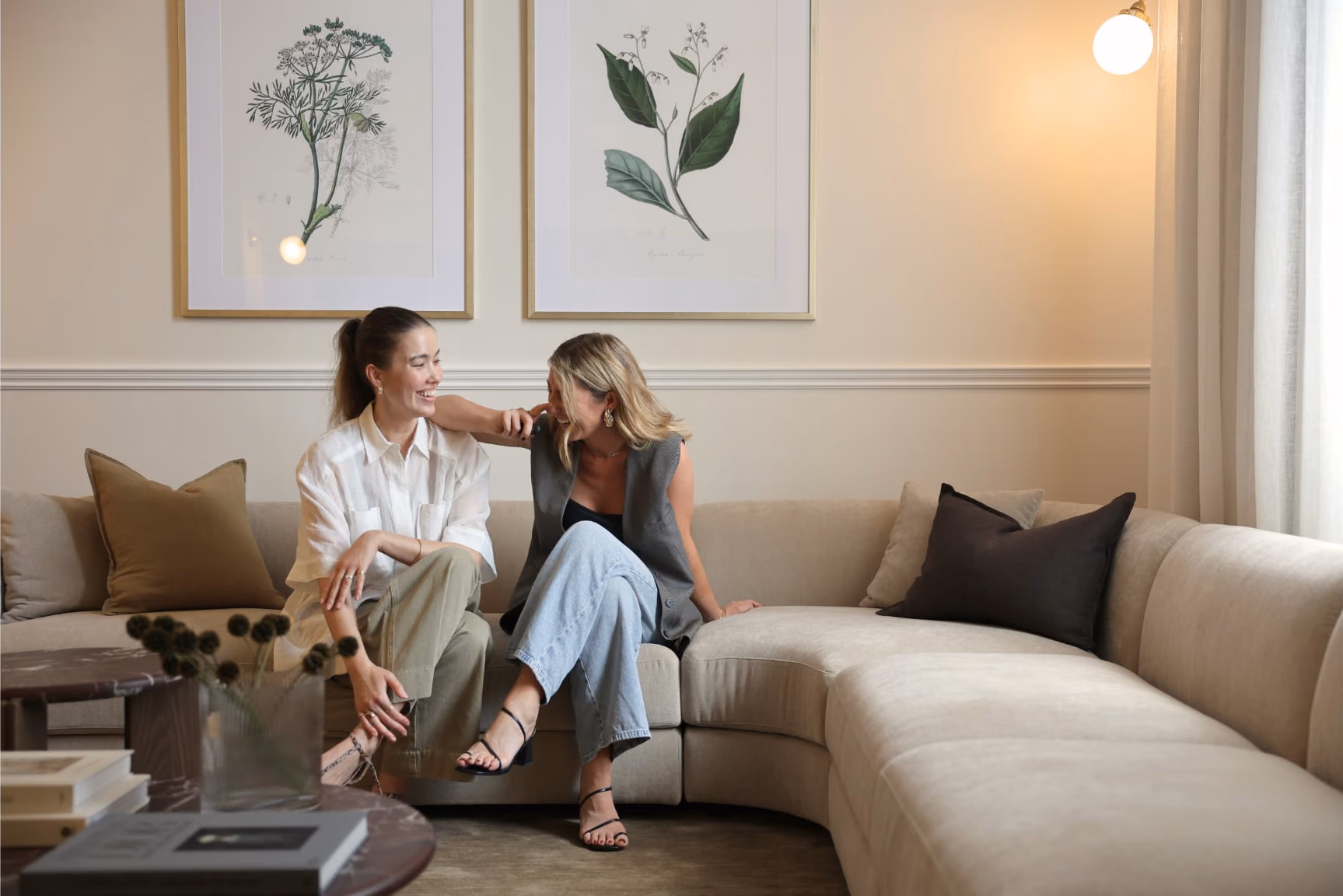 Jessica and Elisha laughing together on the same cream sofa