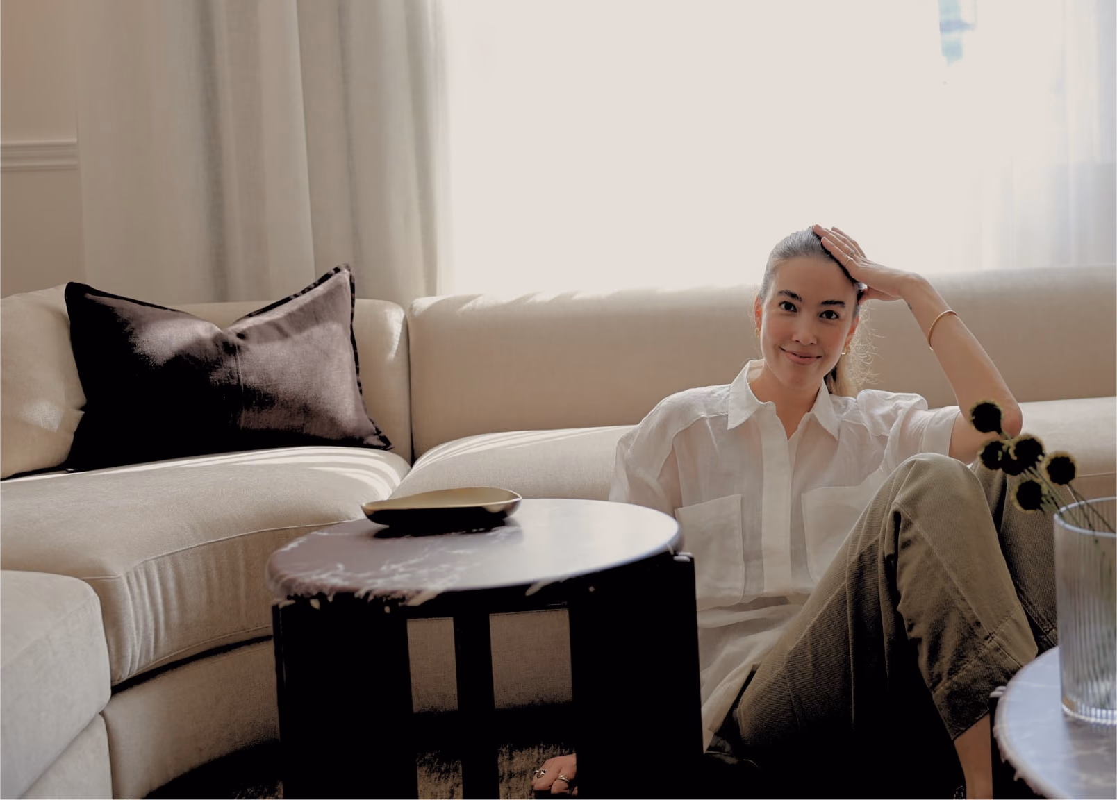 Jessica sitting against a cream sofa beside a marble side table