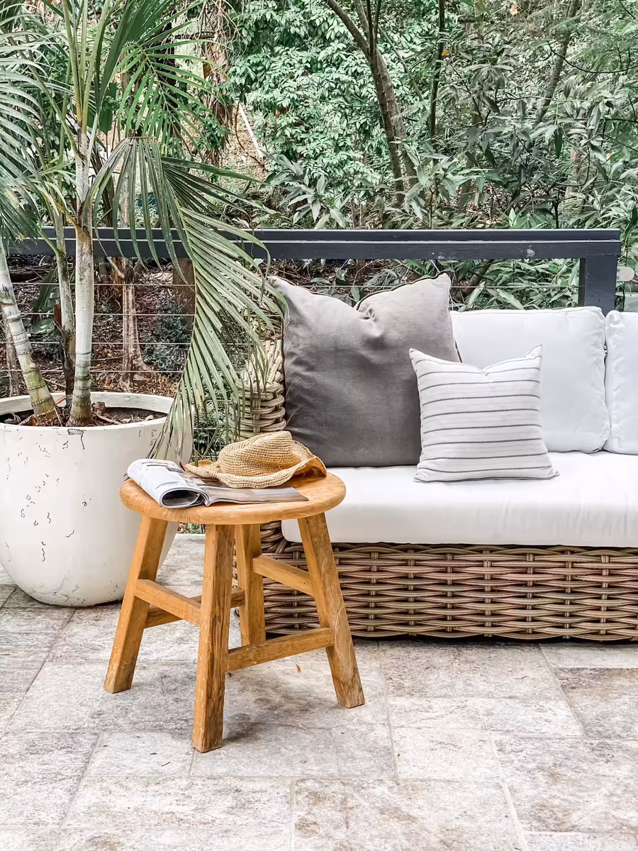 Cushioned wicker outdoor sofa and a timber stool on the travertine terrace, backed by palms
