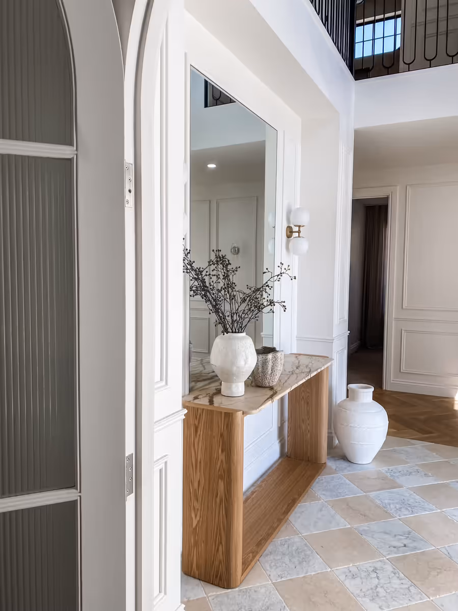 Oak console and mirror seen past fluted joinery, on the checkerboard stone floor