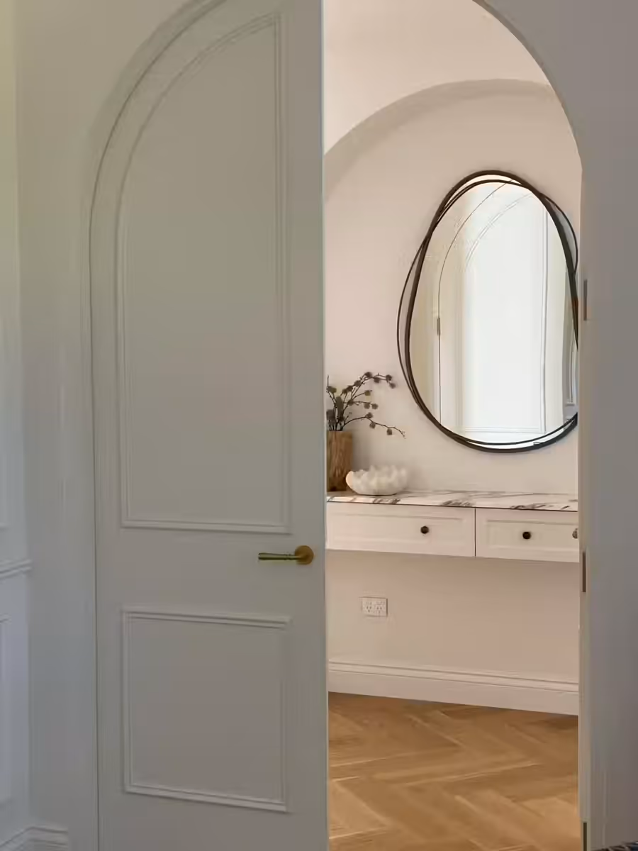 Arched door opening onto the powder room and its organic-edged mirror