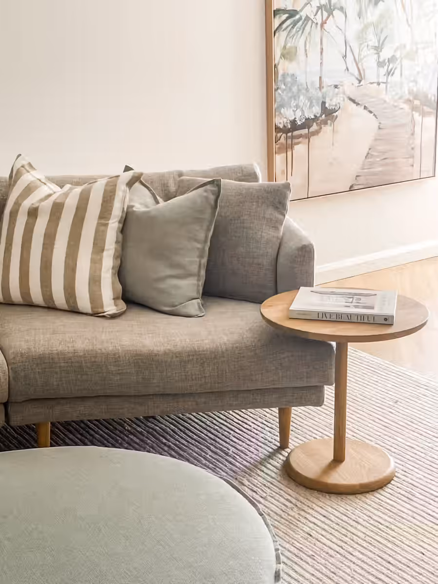 Grey sofa with striped and sage cushions, beside a round oak side table
