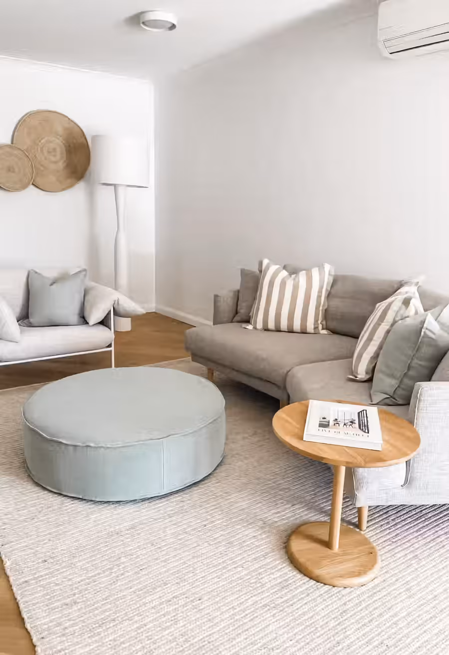 Grey sofa and a sage floor cushion on a wool rug, woven discs hung on the wall