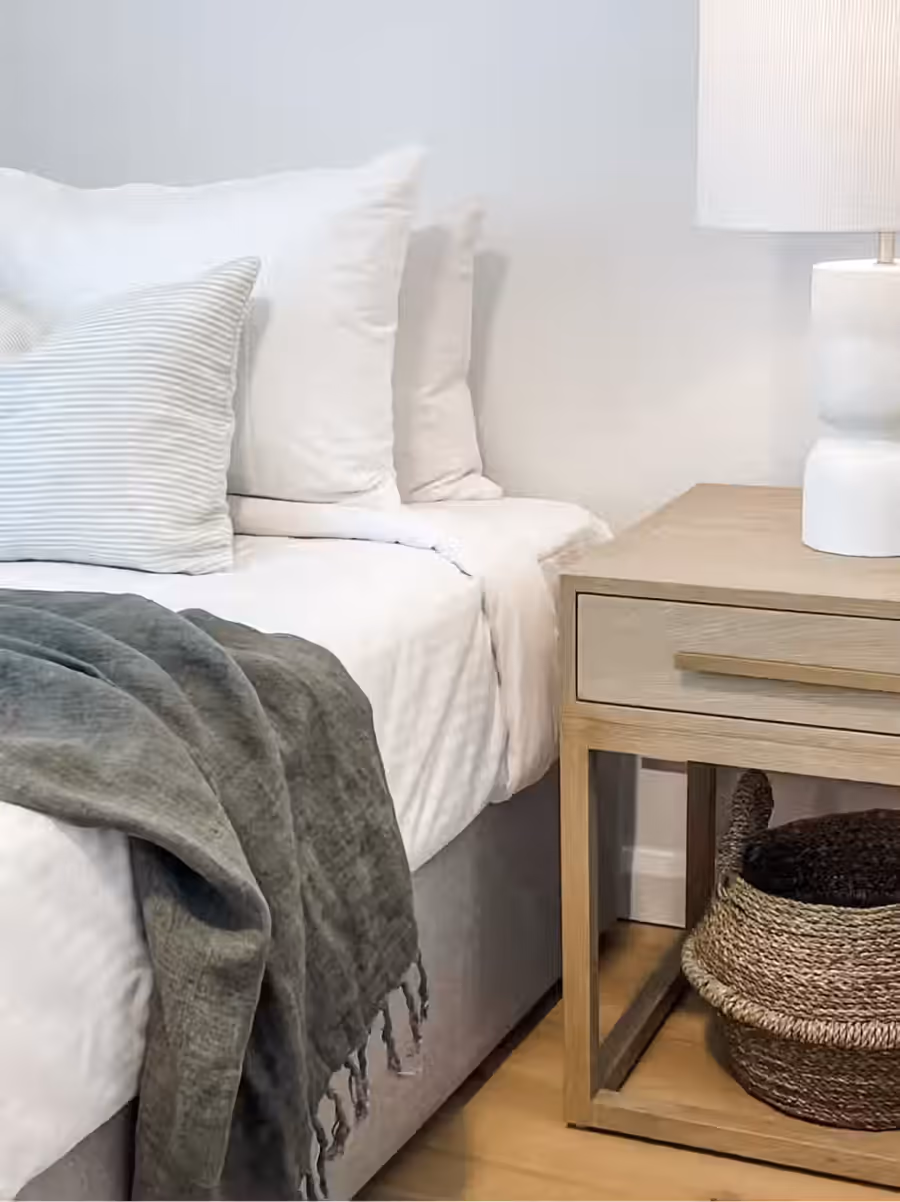 White bedding and a sage throw beside an oak bedside table and basket