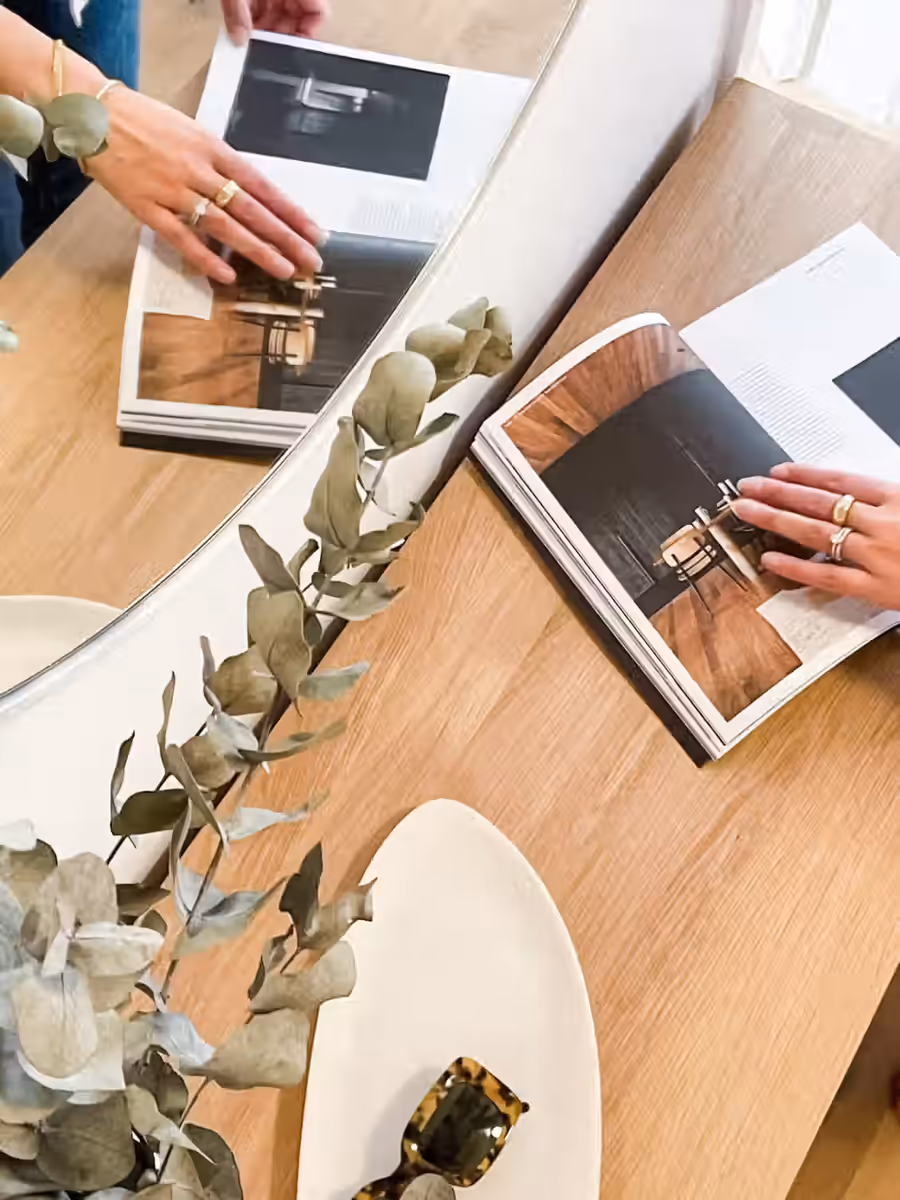 Hands turning the pages of design magazines on the oak table, eucalyptus alongside