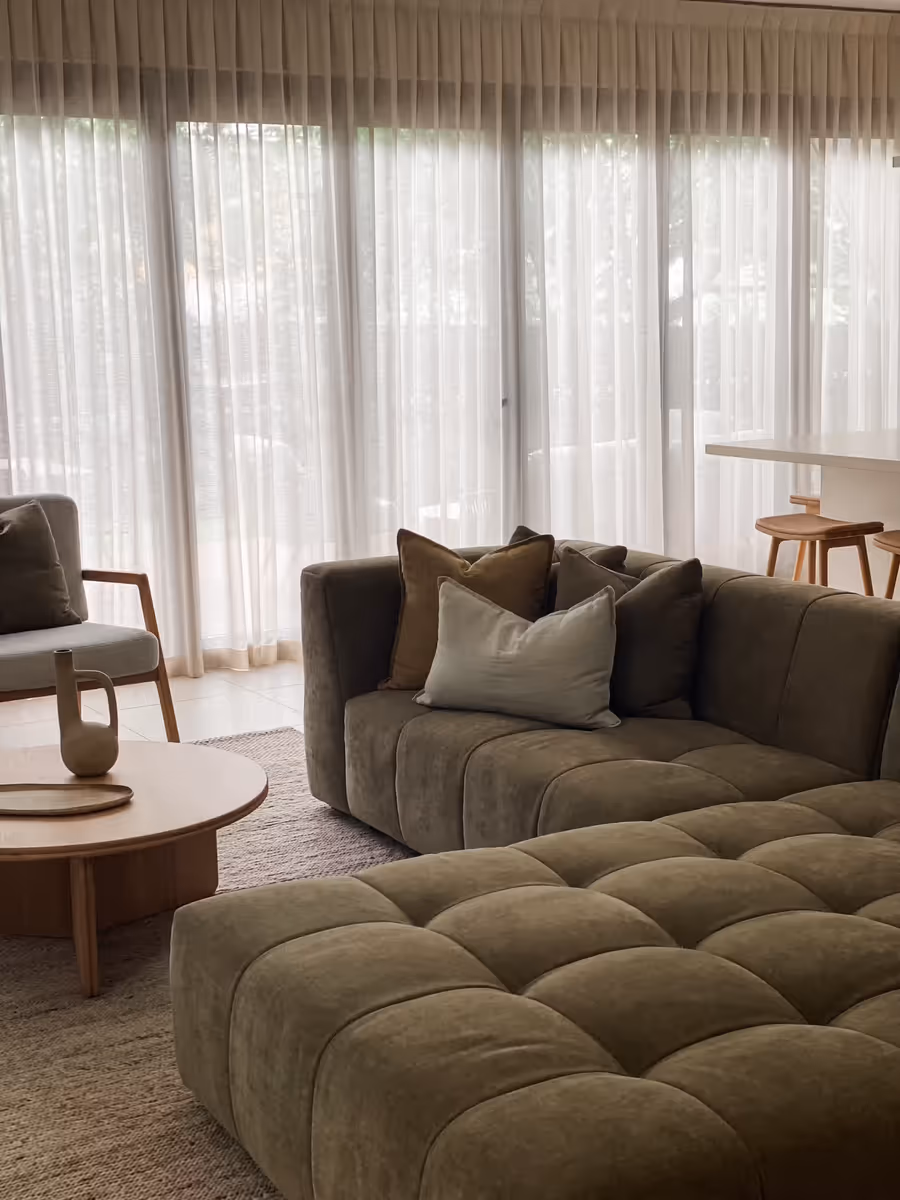 Olive sofa and ottoman against full-width sheers, the dining table beyond