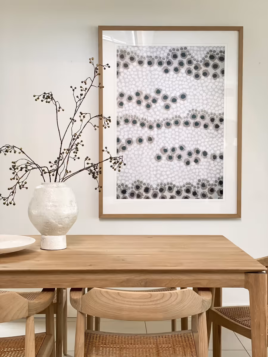 Speckled artwork above the oak dining table, with a textured white vase