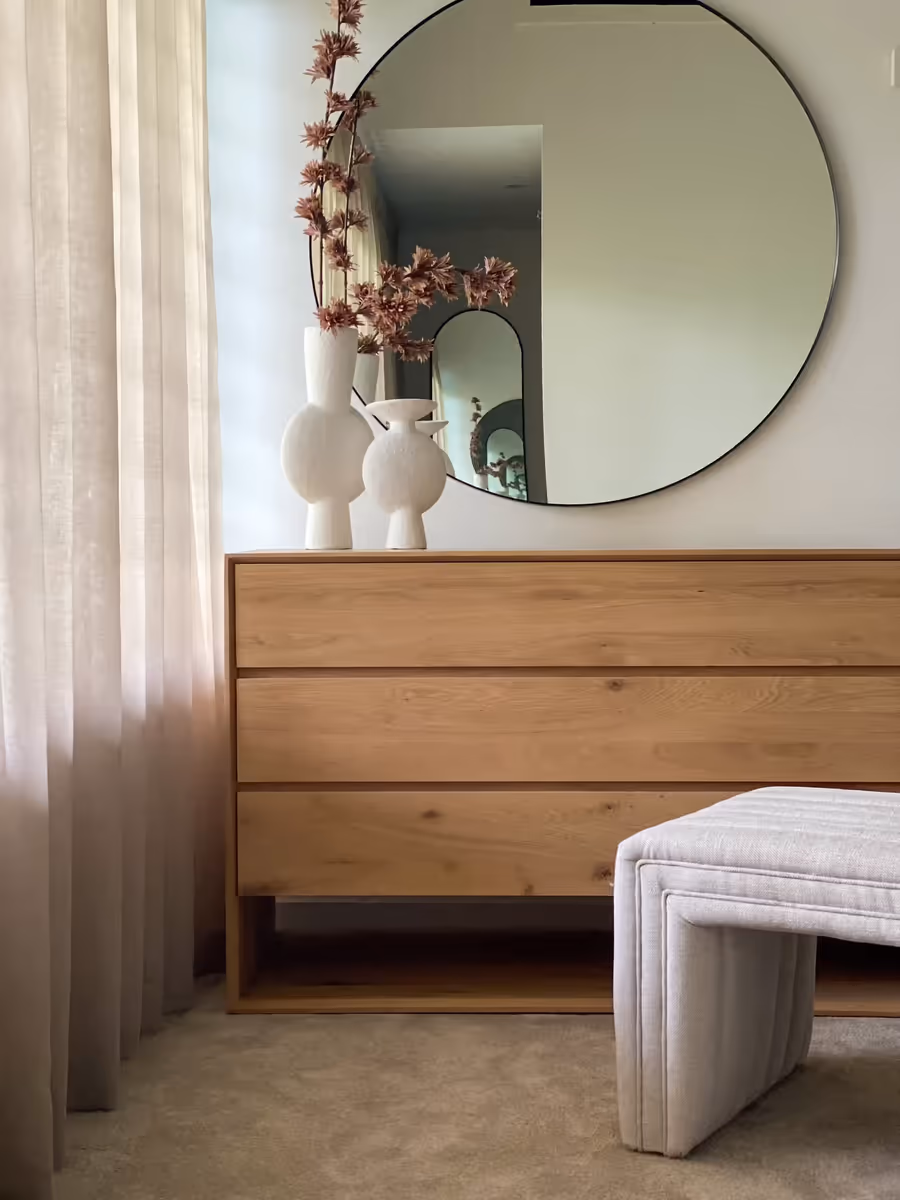 Oak dresser and a stool below a round mirror, vases and blossom on top