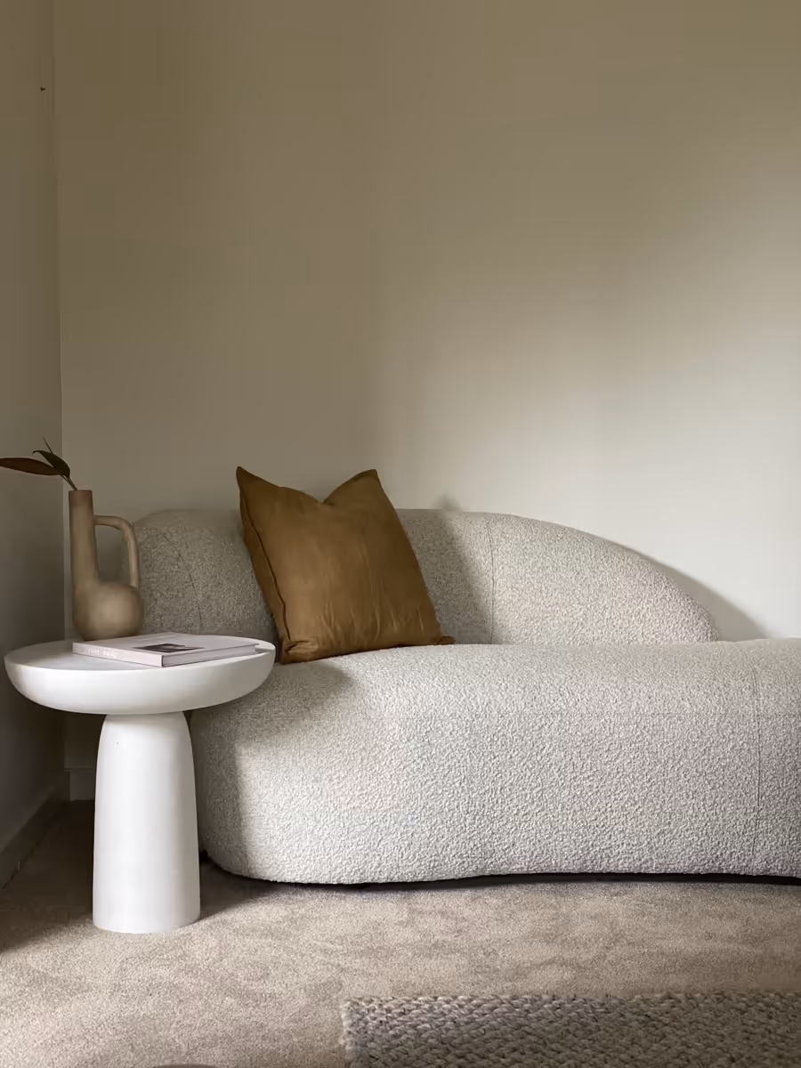 Curved boucle sofa with a mustard cushion, beside a white pedestal side table