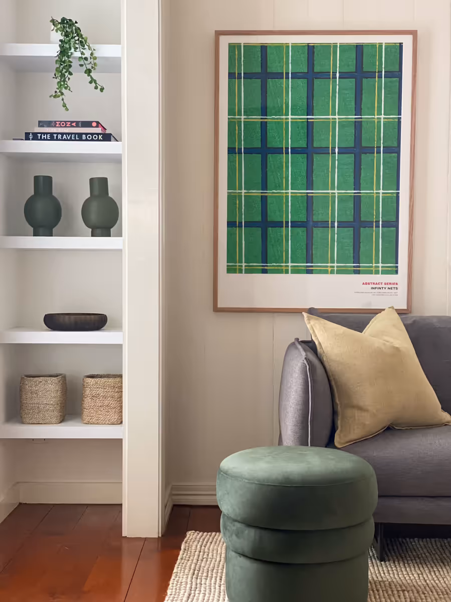 Green plaid artwork beside built-in shelving, with a round olive ottoman